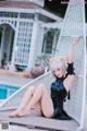 A woman in a black dress sitting on a swing by a pool.