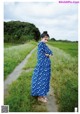 A woman in a blue dress standing on a dirt road.