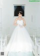 A woman in a wedding dress standing in front of clear chairs.