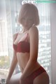 A woman in a red lingerie posing in front of a window.