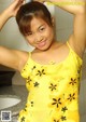 A woman in a yellow top posing in a bathroom.