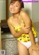 A woman in a yellow top and white panties posing in a bathroom.