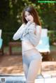 A woman in a white sweater and blue panties posing by a pool.