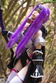 A woman with purple hair holding a sword in the woods.