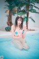 A woman in a bikini sitting in a pool holding an ice cream.