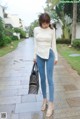 A woman in a white top and blue jeans is walking down a sidewalk.