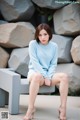 A woman sitting on a bench wearing a blue sweater and white shorts.