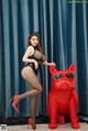 A woman in a black bodysuit and red high heels posing next to a red dog.