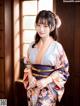 A woman in a kimono standing in front of a window.